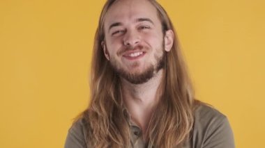 Genç, uzun saçlı, renkli arka planda kameraya gülümseyen bir adam. Çekici sakallı adam mutlu görünüyor.