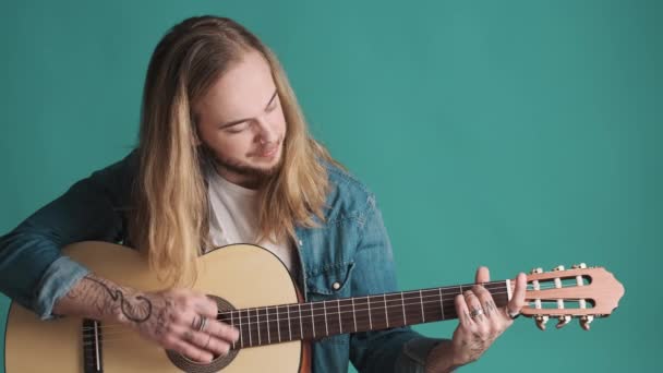 Akustik Gitarla Çalan Uzun Saçlı Genç Adam Mavi Arka Planda — Stok video