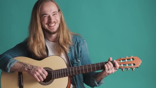 유쾌하게 머리의 남자가 어쿠스틱 기타를 연주하며 배경을 스튜디오에서 즐거운 시간을 — 비디오