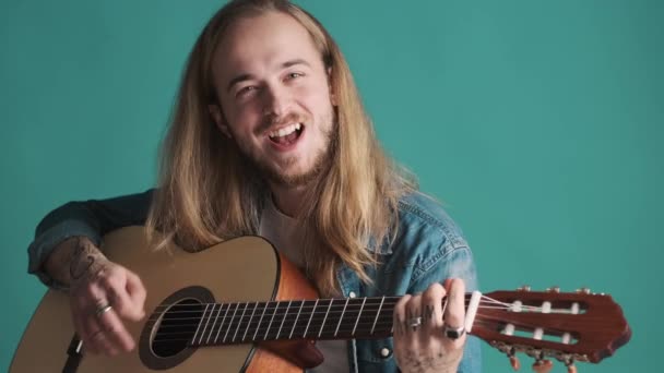 Atrakcyjny Długowłosy Muzyk Wygląda Szczęśliwy Grając Gitarze Śpiewając Niebieskim Tle — Wideo stockowe