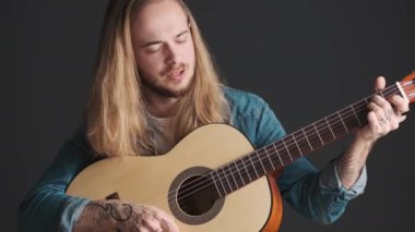 Akustik gitarla çalan yakışıklı, uzun saçlı erkek müzisyen. Gözleri kapalı, siyah arka planda şarkı söylüyor. Müzik aleti konsepti