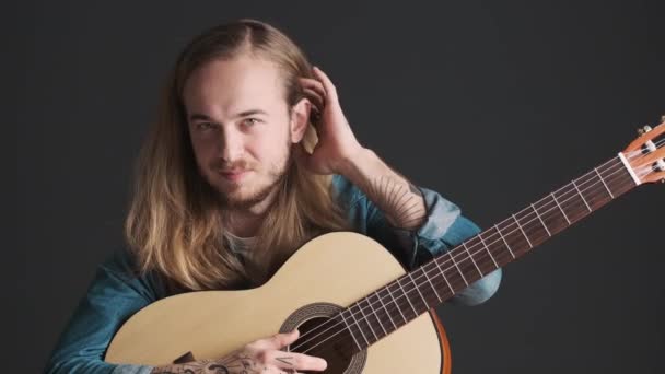 Przystojny Brodaty Muzyk Tulący Włosy Uchem Pozujący Gitarą Przed Kamerą — Wideo stockowe