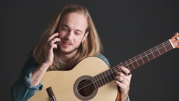 Uzun Saçlı Gitarlı Genç Bir Adam Akıllı Telefondan Arkadaşıyla Konuşuyor — Stok video