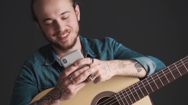 Gitar Çalan Sakallı Genç Bir Adam Akıllı Telefondan Arkadaşıyla Sohbet — Stok video