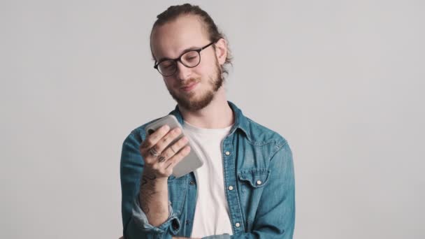 Junger attraktiver bärtiger Mann checkt soziale Netzwerke auf dem Smartphone und lächelt isoliert auf weißem Hintergrund. Modernes Technologiekonzept
