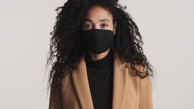 Siyah koruyucu maske takan, beyaz arka planda kendine güvenen genç, çekici bir Afro-Amerikan kadın. Önce güvenlik kavramı