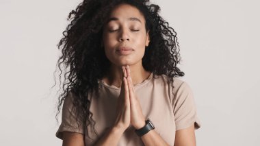 Güzel, siyah tüylü, Afro-Amerikan kadın beyaz arka planda izole edilmiş bir şekilde dua ediyor. Rüyalar gerçek ifade gelebilir.