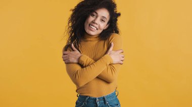 Sarı arka planda kendine sarılan genç Afrikalı Amerikalı kadın. Sana sarılmak istiyorum.