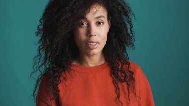 Siyah kabarık saçlı, kırmızı kazaklı, güzel bir Afro kadın. Mavi arka planda, kamerada şehvetli görünüyor.