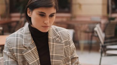 Güzel bir iş kadınının portresi. Samimi bir kafenin avlusunda çalışırken ciddi görünüyor. Yüz ifadesi