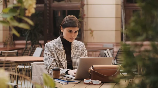 在户外咖啡馆喝咖啡休息时 漂亮时髦的女商人在笔记本电脑上聚精会神地解决工作问题 — 图库照片