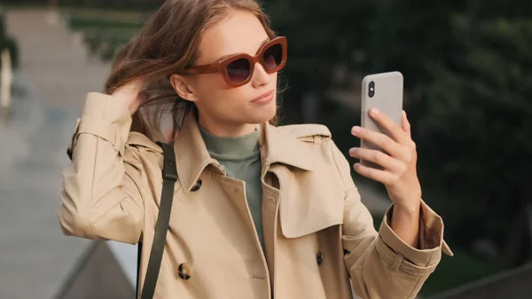 코트를 선글라스를 매력적 여학생 공원을 스마트폰으로 셀카를 — 스톡 사진