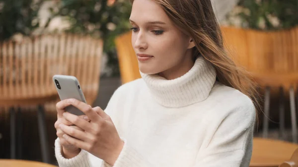 흰색의 스웨터를 아름다운 여학생 온라인 채팅에서 친구들 메시지를 보내며 카페에서 — 스톡 사진