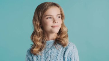 Güzel sarı saçlı, gülümseyen, rahat süveter giyen, mavi arka planda rüya gibi görünen genç kız. Yüz ifadesi