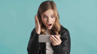 Güzel sarışın genç kız arkadaşlarıyla konuşuyor. Mavi arka planda telefonla görüşüyor. Modern teknoloji kavramı