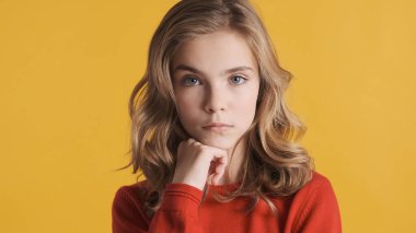 Sarı dalgalı saçlı genç kızın portresi. Elini çenesinin altında tutuyor. Sarı arka planda izole edilmiş düşünceli görünüyor.