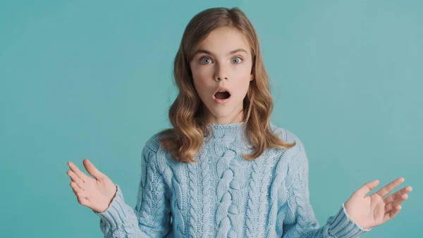 Portrait of blond teenager girl with open mouth looking amazed isolated on blue background. Wow expression