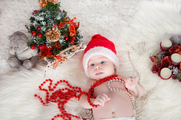 Χαριτωμένο μωρό στο santa καπέλο που βρίσκεται στο χαλί κοντά το χριστουγεννιάτικο δέντρο — Φωτογραφία Αρχείου