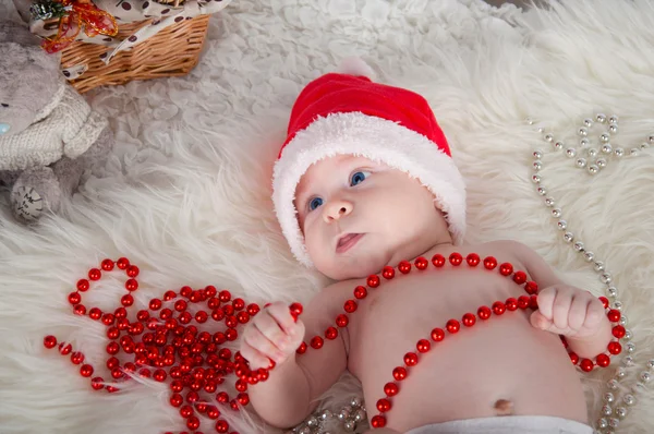 Söt baby i santa hatt ligger på mattan nära julgranen — Stockfoto