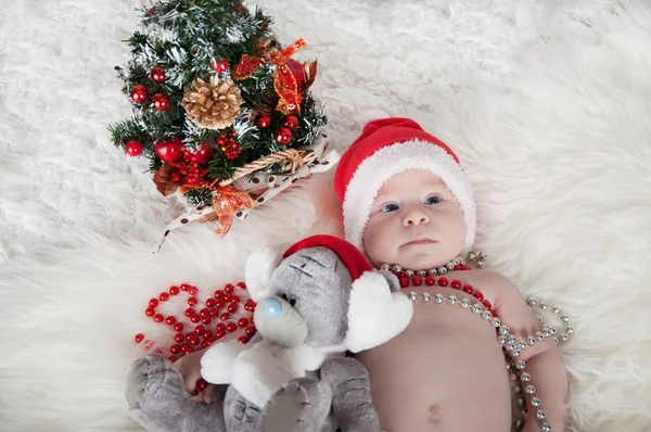 Söt baby i santa hatt ligger på mattan nära julgranen — Stockfoto