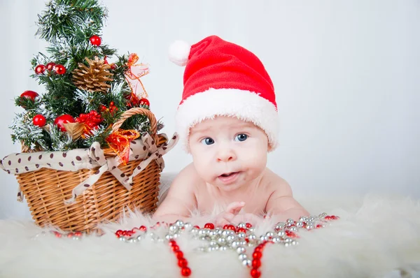Χαριτωμένο μωρό στο santa καπέλο που βρίσκεται στο χαλί κοντά το χριστουγεννιάτικο δέντρο — Φωτογραφία Αρχείου