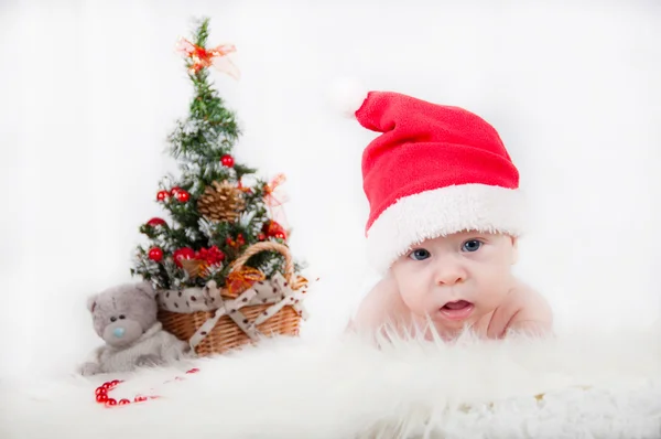 Bébé mignon dans le chapeau du Père Noël avec un arbre de Noël derrière — Photo