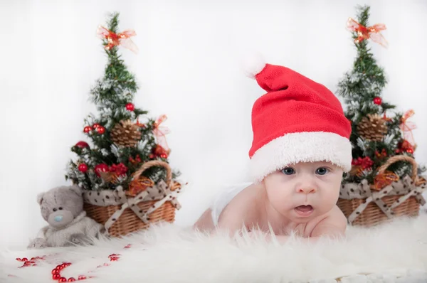 Lindo bebé en el sombrero de Santa con un árbol de Navidad detrás —  Fotos de Stock