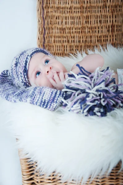 Newborn baby lies in basket in a multi color hat on white background. — Stock Photo, Image