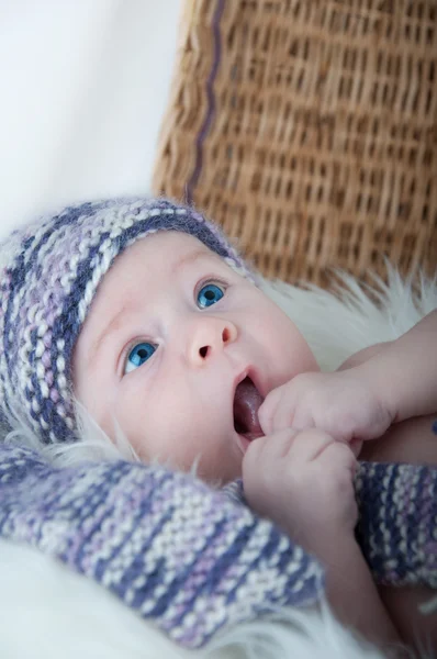 Newborn baby lies in basket in a multi color hat on white background. — Stock Photo, Image