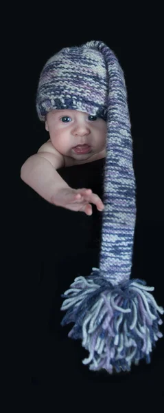 Nouveau-né dans un long chapeau multicolore regardant la caméra sur un fond noir — Photo
