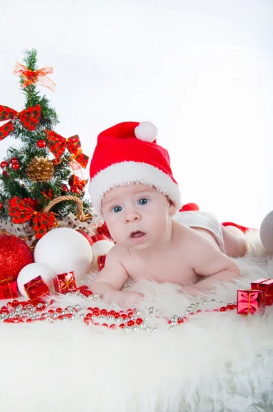 Симпатичный малыш в шляпе Санты с рождественской елкой позади — стоковое фото