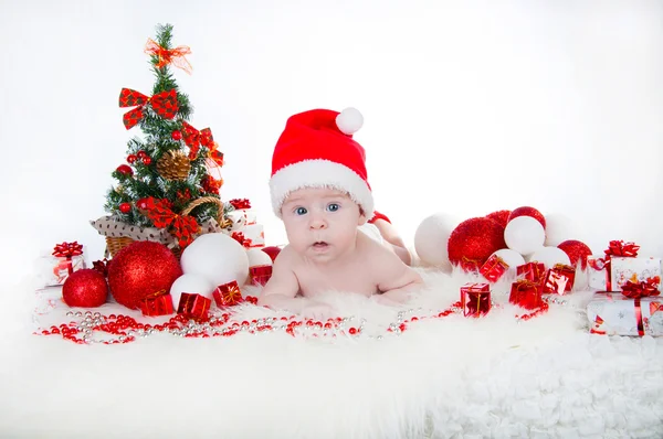 Niedliches Baby mit Weihnachtsmütze und einem Weihnachtsbaum dahinter — Stockfoto