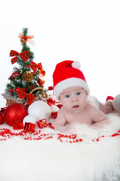Schattige baby in kerstmuts met een kerstboom achter — Stockfoto