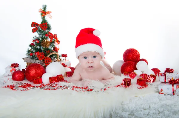 Niedliches Baby mit Weihnachtsmütze und einem Weihnachtsbaum dahinter — Stockfoto