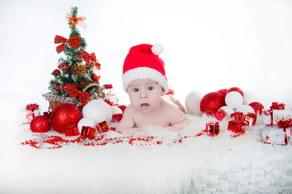 Söt baby i Tomtemössa med en julgran bakom — Stockfoto