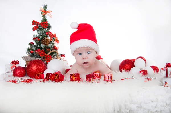 Söt baby i Tomtemössa med en julgran bakom — Stockfoto