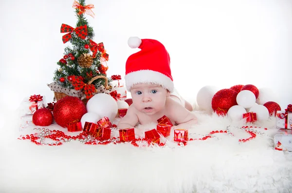Schattige baby in kerstmuts met een kerstboom achter — Stockfoto