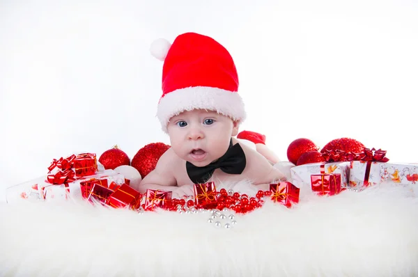 Niedliches Baby mit Weihnachtsmütze und schwarzer Fliege neben dem Weihnachtsbaum — Stockfoto