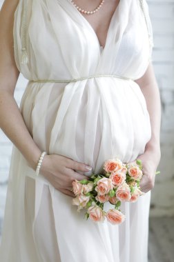 Closeup uzun beyaz elbise giyiyordu, eller buket gül çiçek içinde tutan hamile kadın, karın üzerinde
