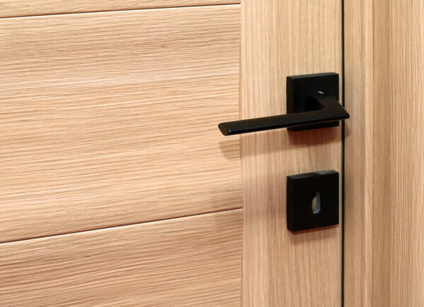 Закрытая бежевая деревянная дверь внутри с черной ручкой