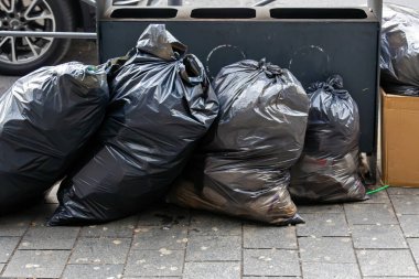 Şehir sokağında plastik çöp torbaları yığını var.