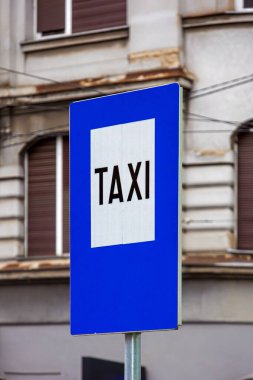 Şehir caddesinde üzerinde beyaz Taxi yazan mavi bilgi levhası.