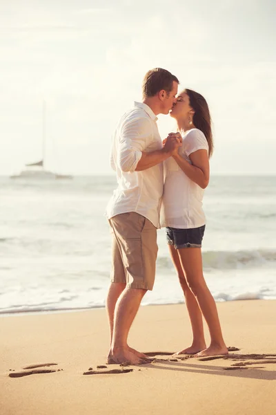 Молодая пара целуется на пляже на закате — стоковое фото