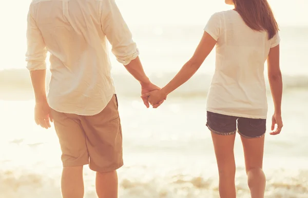 Jovem casal de mãos dadas na praia ao pôr do sol — Fotografia de Stock