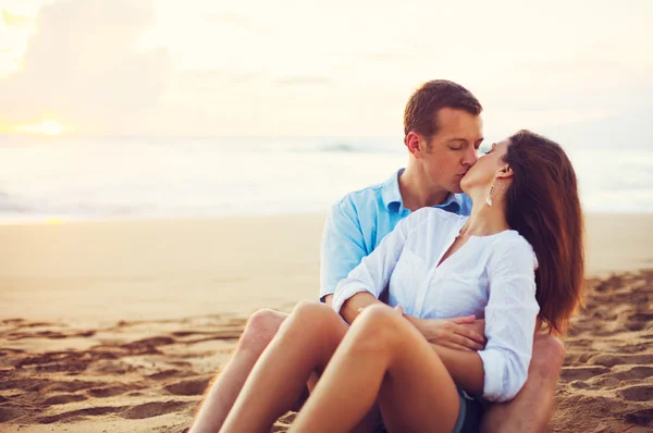 Paar ontspannen op het strand zoenen en kijken naar de zonsondergang — Stockfoto