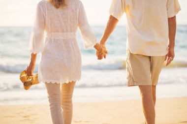 Olgun çift gün batımında sahilde yürüyüş