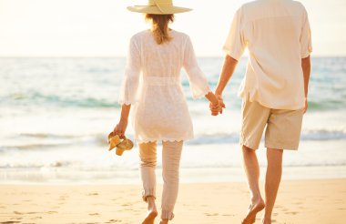 Olgun çift gün batımında sahilde yürüyüş