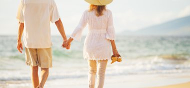 Olgun çift gün batımında sahilde yürüyüş