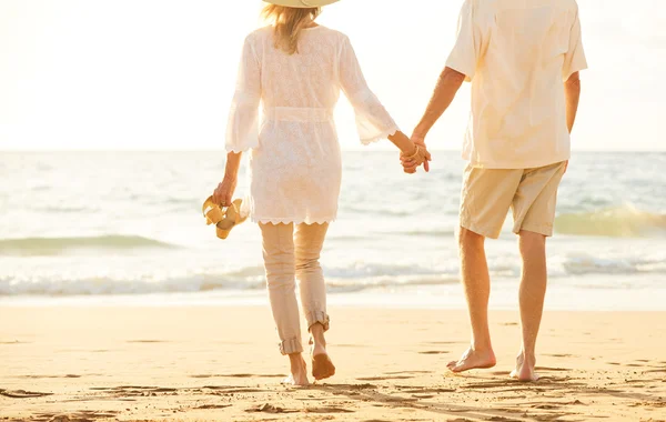 Pareja madura caminando en la playa al atardecer —  Fotos de Stock