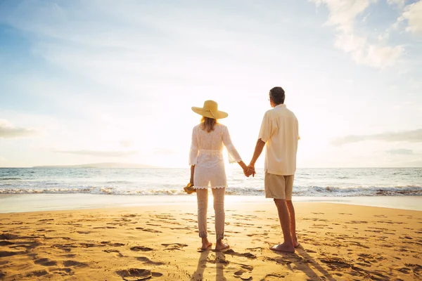 Pareja madura caminando en la playa al atardecer —  Fotos de Stock